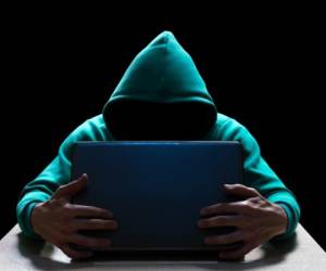 Unknown person in the hood, reaches out from the darkness to the laptop. Theft of household and computer equipment.