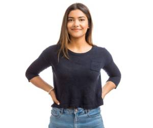 Portrait of female brunette in blue top standing against white background