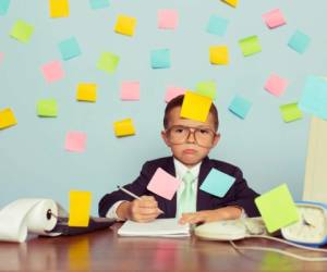 A young businessman sitting at his office computer with pen in hand is completely covered with blank sticky notes. He is forgetting many tasks for his business operations. He wearing a suit and tie and has a frustrated look on his look on his face.