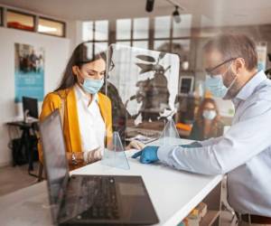 Bank teller discussing paperwork with customer at bank counter wearing protective gloves and face mask. Office with acrylic glass partition on desk. Acrylic glass wall - protection against coughs and spitting, protection against viruses.