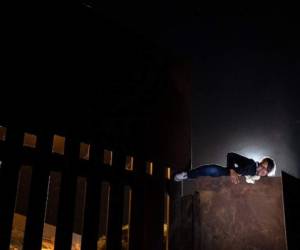 A woman who has been traveling in a caravan of Central American migrants hoping to get to the United States, climbs the metal barrier separating Mexico and the US to cross from Playas de Tijuana in Mexico into the US, on December 3, 2018. - Thousands of Central American migrants, mostly Hondurans, have trekked for over a month in the hopes of reaching the United States. (Photo by Guillermo Arias / AFP)