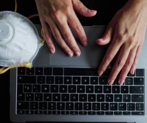 Closeup image of a woman working and typing on laptop computer keyboard with a mask during coronavirus crisis