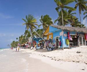 Punta Cana, Dominican Republic- July 20, 2013: Tourist walking on the beach and take a tour of the bungalows-stalls with souvenirs. Locals sitting in front of stalls