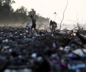 Personas caminan entre residuos plásticos y otros desechos en una playa de Omoa, Honduras, el 10 de septiembre de 2022. - Arrastrados por diferentes afluentes, inmensos depósitos de plástico multicolor cubren como un manto las tranquilas aguas del lago de Suchitlán en El Salvador. Lo mismo sucede en las paradisíacas playas del Caribe hondureño, que reciben miles de toneladas de desechos de Guatemala. (Foto por ORLANDO sierra / AFP)