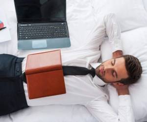 Top view of handsome young man in shirt and tie holding hands behind head and keeping eyes closed while lying in bed at the hotel room