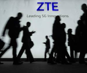 People walk in front of the ZTE stand at the Mobile World Congress (MWC), the world's biggest mobile fair, on February 27, 2018 in Barcelona. - The Mobile World Congress is held in Barcelona from February 26 to March 1. (Photo by LLUIS GENE / AFP)