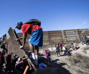 A group of Central American migrants -mostly Hondurans- climb a metal barrier on the Mexico-US border near El Chaparral border crossing, in Tijuana, Baja California State, Mexico, on November 25, 2018. - US officials closed the San Ysidro crossing point in southern California on Sunday after hundreds of migrants, part of the 'caravan' condemned by President Donald Trump, tried to breach a fence from Tijuana, authorities announced. (Photo by Pedro PARDO / AFP)