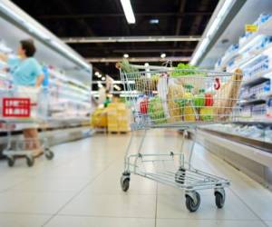 Shopping cart full of grocery standing next to shelves with dairy products in hypermarket