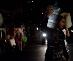 People queue for drinking water (L) being distributed in a tanker in the municipality of Chacao in a tanker, in Caracas, on March 11, 2019. - Venezuela President Nicolas Maduro extended the closure of shools and businesses for another 24 hours on Monday due to the ongoing electricity blackout, Communications Minister Jorge Rodriguez said. The power outage caused chaos with public services such as water and transport also grinding to a halt, while hospitals were left without power. (Photo by Cristian HERNANDEZ / AFP)