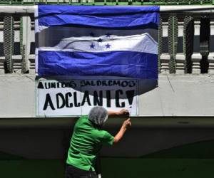 A man places a Honduran national flag and a sign reading 'United we will succeed' on the balcony of a supermarket in Tegucigalpa on April 18, 2020, amid the new coronavirus pandemic. - 46 have died out of 457 infected with COVID-19 in Honduras since the outbreak in its Central American nation. (Photo by ORLANDO SIERRA / AFP)