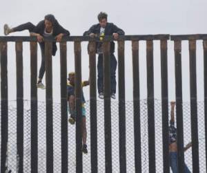 Migrant caravan demonstrators climb the US-Mexico border fence during a rally, on April 29, 2018, in San Ysidro, California.The US has threatened to arrest around 100 Central American migrants if they try to sneak in from the US-Mexico border where they have gathered, prompting US President Donald Trump to order troop reinforcements on the frontier. / AFP PHOTO / Sandy Huffaker