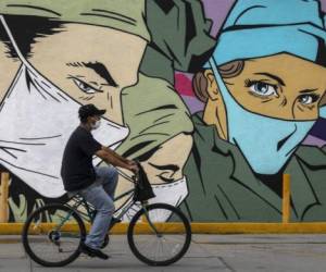 A man ride sa bike past a coronavirus-related mural by urban artists Mick Martinez and 'Were Torres' in Ciudad Juarez, Chihuahua state, Mexico, on June 27, 2020. (Photo by HERIKA MARTINEZ / AFP)
