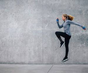 Side view shot of fit young woman doing cardio interval training against grey background. Fitness female exercising outdoors in morning.