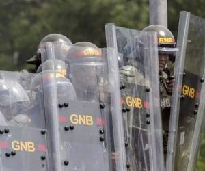 Miembros de la Guardia Nacional Bolivariana se protegen de las piedras que lanzan los manifestantes en la frontera con Brasil, el domingo.