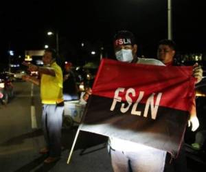 Supporters of Nicaragua's President Daniel Ortega and vice presidential candidate, his wife, Rosario Murillo, hold up a flag of the Sandinista National Liberation Front (FSLN) while celebrating after preliminary results showed Ortega is expected to be re-elected, at Victoria Square in Managua on November 7, 2021. (Photo by OSWALDO RIVAS / AFP)