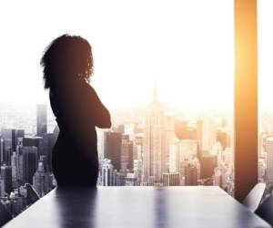 Silhouetted shot of a young businesswoman looking at a cityscape from an office window