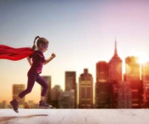 Little child girl plays superhero. Child on the background of sunset sky. Girl power concept