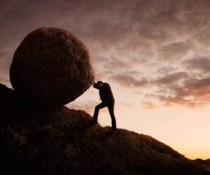 Silhouette of young businessman pushing large stone uphill with copy space