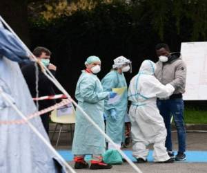 Hospital employees wearing a protection mask and gear tend to a patient (R) coming in to be tested at a temporary emergency structure set up outside the accident and emergency department, where any new arrivals presenting suspect new coronavirus symptoms are being tested, at the Brescia hospital, Lombardy, on March 13, 2020. (Photo by Miguel MEDINA / AFP)