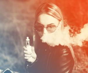 blonde girl vaping outdoors . female model smoking fruit flavored e-liquid or e-juice with vaporizer device or e-cig.Modern gadget for smokers