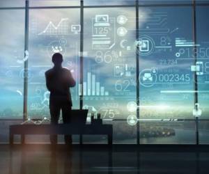 A silhouette of a man stands on the background of large office windows and views a hologram of corporate infographic with work data.