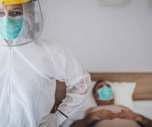 Man and woman, senior man lying in hospital bed because of coronavirus infection, female doctor in standing next to him.