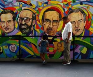 A man and a girl stand in front of a mural in homage of six Jesuit priests and two employees murdered during the civil war on the 30th anniversary of the crime in San Salvador, on November 16, 2019. - Six Spanish Jesuit priests and two employees were murdered by government military forces on November 16, 1989, during the Salvadoran Civil War. (Photo by Marvin RECINOS / AFP)