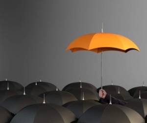 Business Man holding orange colored umbrella between the black umbrellas