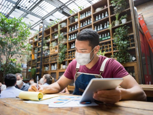 Portrait of a business manager doing the books at a restaurant wearing a facemask during the COVID-19 pandemic - reopening of business