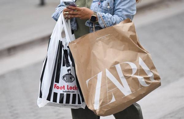 <i>Un comprador usa un iPhone de Apple mientras lleva bolsas de compras de Foot Locker y Zara mientras camina por Third Street Promenade en Santa Mónica, California, el 20 de marzo de 2023. FOTO Patrick T. Fallon / AFP</i>