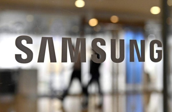 People walk past the Samsung logo displayed on a glass door at the company's Seocho building in Seoul on January 7, 2022, after South Korean tech giant Samsung Electronics expected its operating profits for the fourth quarter to soar 52.5 percent. (Photo by Jung Yeon-je / AFP)