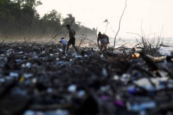 Personas caminan entre residuos plásticos y otros desechos en una playa de Omoa, Honduras, el 10 de septiembre de 2022. - Arrastrados por diferentes afluentes, inmensos depósitos de plástico multicolor cubren como un manto las tranquilas aguas del lago de Suchitlán en El Salvador. Lo mismo sucede en las paradisíacas playas del Caribe hondureño, que reciben miles de toneladas de desechos de Guatemala. (Foto por ORLANDO sierra / AFP)