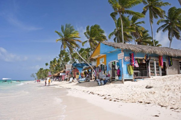 Punta Cana, Dominican Republic- July 20, 2013: Tourist walking on the beach and take a tour of the bungalows-stalls with souvenirs. Locals sitting in front of stalls
