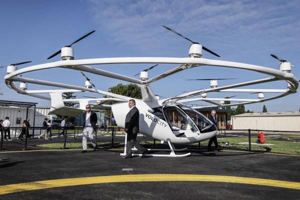 <i>Varias personas se encuentran junto a un taxi volador Volocopter Volocity en el aeródromo de Saint-Cyr-l'École, Francia, el 8 de agosto de 2024, para conmemorar la inauguración del primer vertiport, una pista de despegue y aterrizaje para taxis. Foto de Thibaud MORITZ/AFPThibaud MORITZ / AFP</i>