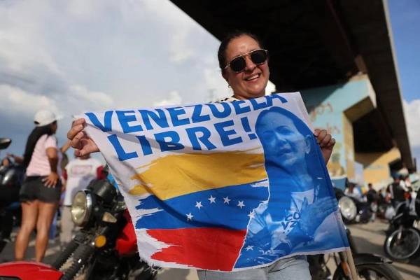 <i>Una mujer sostiene una bandera mientras espera la llegada de la líder opositora y premio nobel de la paz 2025, en Maracay (Venezuela). EFE/ Miguel Gutiérrez</i>