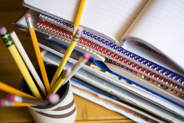 Stack of books or paperwork on desk. High angle view, pencils in holder in foreground.
