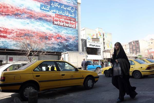 <i>Una mujer iraní pasa frente a un cartel antiestadounidense en Teherán, Irán, el 25 de febrero de 2026. Irán y Estados Unidos mantienen este jueves una tercera ronda de negociaciones en Ginebra en busca de un acuerdo nuclear en medio de las amenazas de una intervención armada del presidente estadounidense, Donald Trump, quien ha realizado el mayor despliegue militar en Oriente Medio desde la guerra de Irak. EFE/EPA/ABEDIN TAHERKENAREH</i>