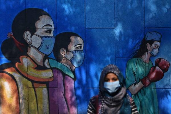 <i>Una mujer que lleva una mascarilla como medida preventiva contra el coronavirus COVID-19 pasa junto a un mural pintado en una pared. Foto de Sajjad HUSSAIN / AFP / ARCHIVO E&amp;N</i>