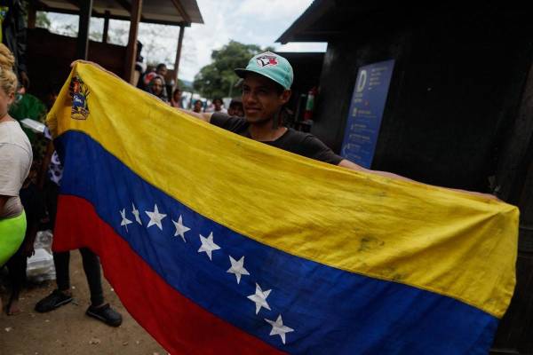 <i>Un migrante venezolano sostiene la bandera venezolana durante su estancia en la Estación de Recepción de Migrantes en Lajas Blancas, Provincia de Darién, Panamá, el 6 de octubre de 2023. FOTO ROBERTO CISNEROS/AFP</i>