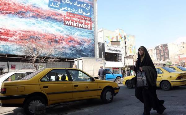 <i>Una mujer iraní pasa frente a un cartel antiestadounidense en Teherán, Irán, el 25 de febrero de 2026. Irán y Estados Unidos mantienen este jueves una tercera ronda de negociaciones en Ginebra en busca de un acuerdo nuclear en medio de las amenazas de una intervención armada del presidente estadounidense, Donald Trump, quien ha realizado el mayor despliegue militar en Oriente Medio desde la guerra de Irak. EFE/EPA/ABEDIN TAHERKENAREH</i>