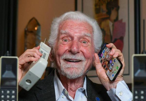 <i>El ingeniero Martin Cooper sostiene en su mano derecha una copia contemporánea del teléfono celular original que usó para hacer la primera llamada telefónica el 3 de abril de 1973, en Del Mar, California, el 20 de marzo de 2023. - (Foto de VALERIE MACON / AFP )</i>