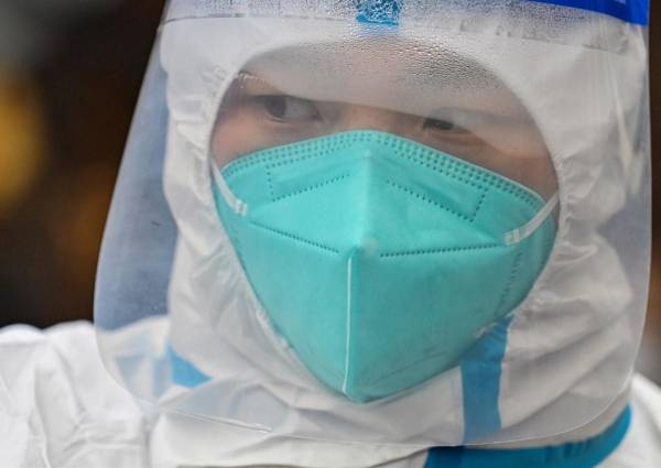 <i>Un trabajador con equipo de protección observa cómo se realiza la prueba del coronavirus Covid-19 a las personas en un complejo residencial en Shanghai. FOTO Héctor RETAMAL / AFP</i>