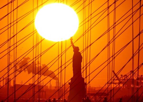 <i>El sol se pone detrás de la Estatua de la Libertad mientras la gente camina por el puente de Brooklyn en Nueva York el 6 de febrero de 2024. FOTO Charly TRIBALLEAU / AFP</i>