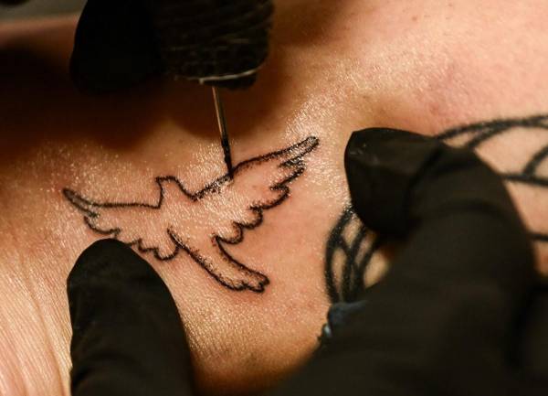 <i>La tatuadora Kat Dukes le hace un tatuaje de una paloma a mano a Scout Frank usando tinta mezclada con las cenizas de la madre cremada de Frank, Theresa Pendleton, en Oceanside, California, el 6 de octubre de 2023. FOTO PATRICK T. FALLON / AFP</i>
