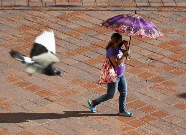 <i>Una mujer se protege del sol con una sombrilla mientras camina por la plaza principal de Comayagua, Honduras, el 27 de febrero de 2024, mientras una ola de calor azota el país. FOTO Orlando SIERRA/AFP</i>