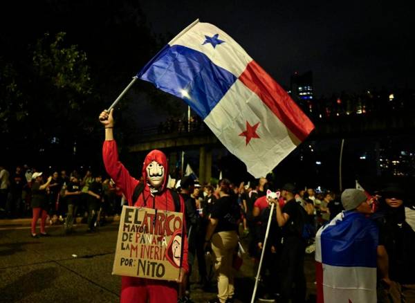 Un manifestante con una máscara y un traje de Money Heist ondea una bandera panameña durante una marcha contra el contrato gubernamental con la compañía minera canadiense First Quantum y su filial Minera Panamá en la ciudad de Panamá el 27 de octubre de 2023. FOTO LUIS ACOSTA / AFP