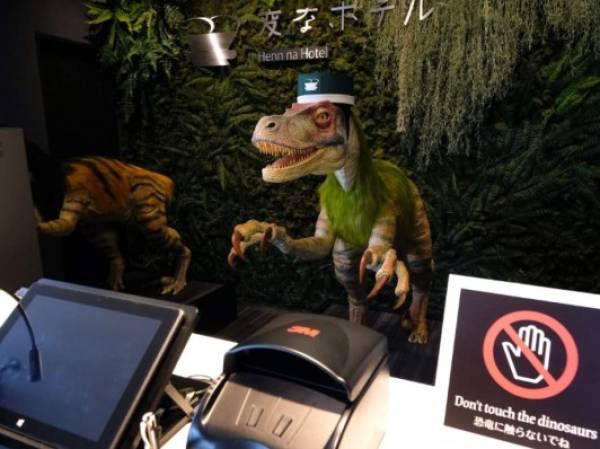 A robot dinosaur wearing a bellboy hats welcomes guests from the front desk at the Henn-na Hotel in Urayasu, suburban Tokyo on August 31, 2018. The reception at the Henn-na Hotel east of Tokyo is eeriely quiet until customers near the robot dinosaurs manning front desk. Their sensors detect motion and they bellow: 'Welcome.' It might be about the weirdest check-in experience possible, but that's exactly the point at the Henn-na ('Weird') chain, which bills itself as offering the world's first hotels staffed by robots. / AFP PHOTO / Kazuhiro NOGI