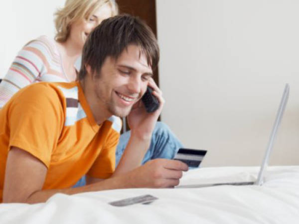 Couple on bed by laptop, man holding credit card and using telephone