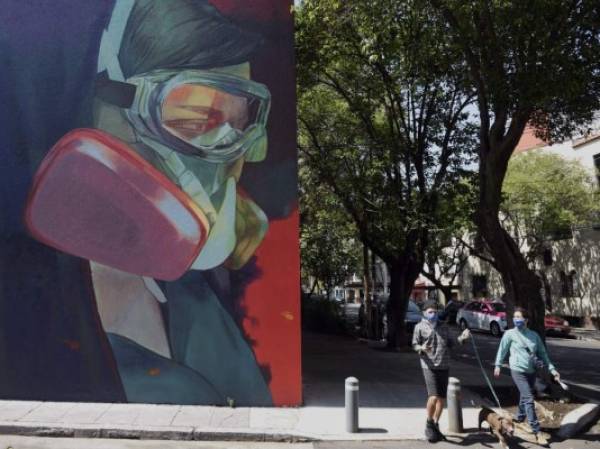 People walk next to a coronavirus-related mural at the Roma neighborhood in Mexico City, on June 9, 2020, during the novel COVID-19 pandemic. (Photo by ALFREDO ESTRELLA / AFP)