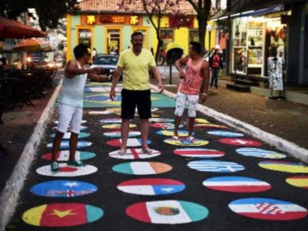 Personas posan en una calle pintada con las banderas de las selecciones que toman parte del Mundial-2014, el 11 de junio en Itu. (Foto: AFP).